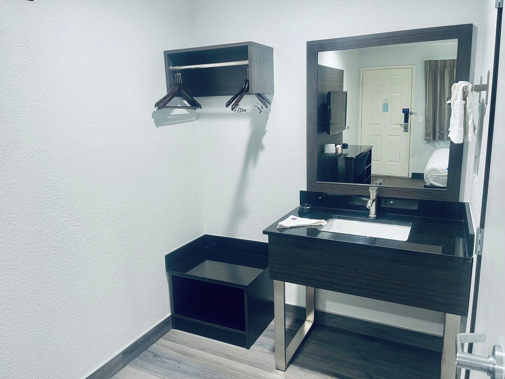 A modern bathroom with a dark vanity, a mirror, a towel rack, and a small shelf.