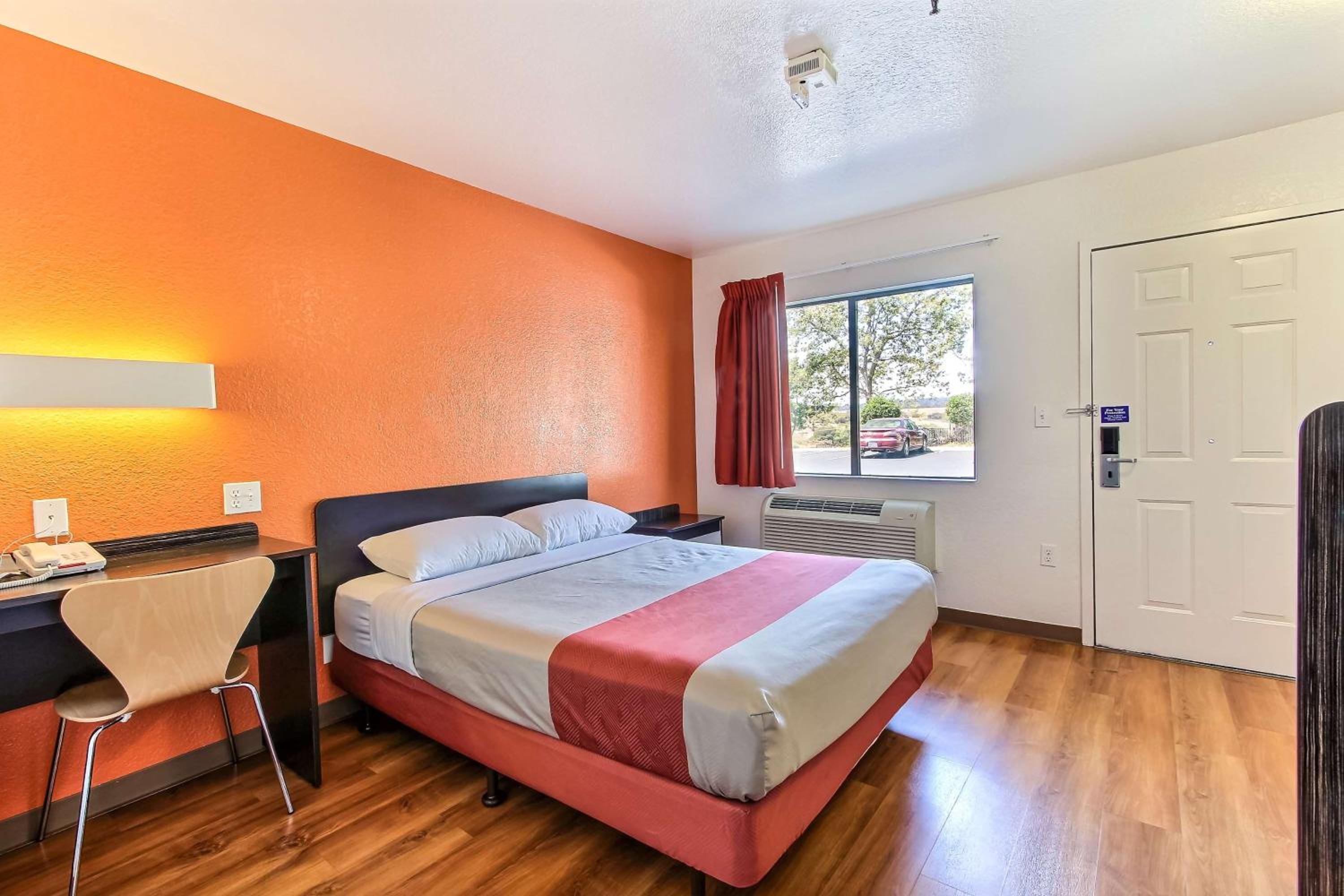 A hotel room with a bed, desk, chair, window, and door.