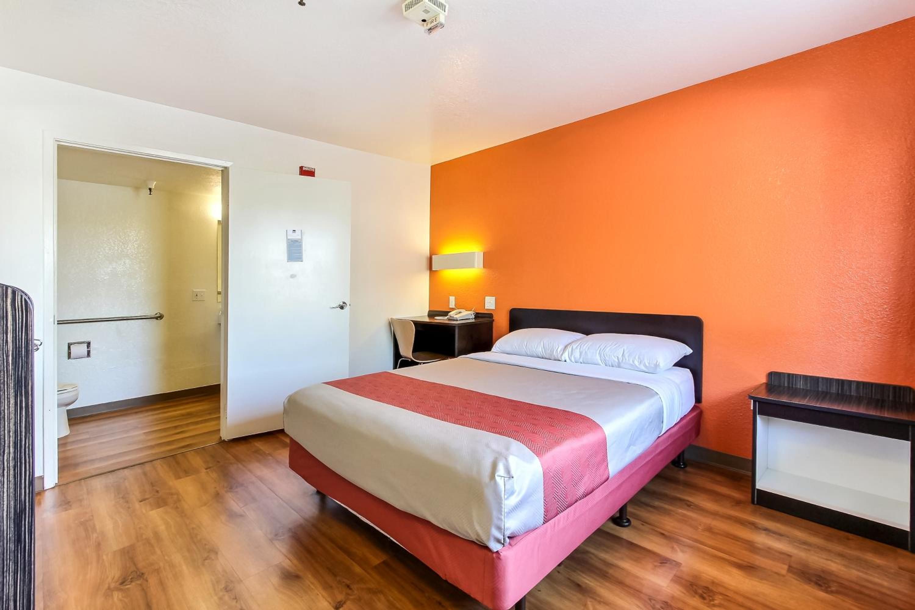 A hotel room with a bed, a desk, a chair, and a nightstand.