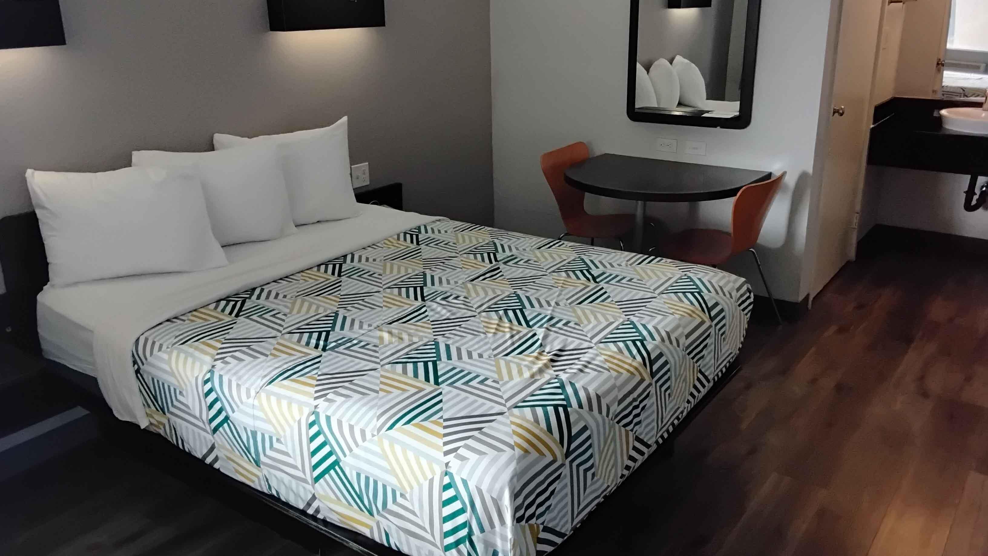 A neatly made bed with a patterned bedspread, a small table with a chair, and a mirror on the wall.