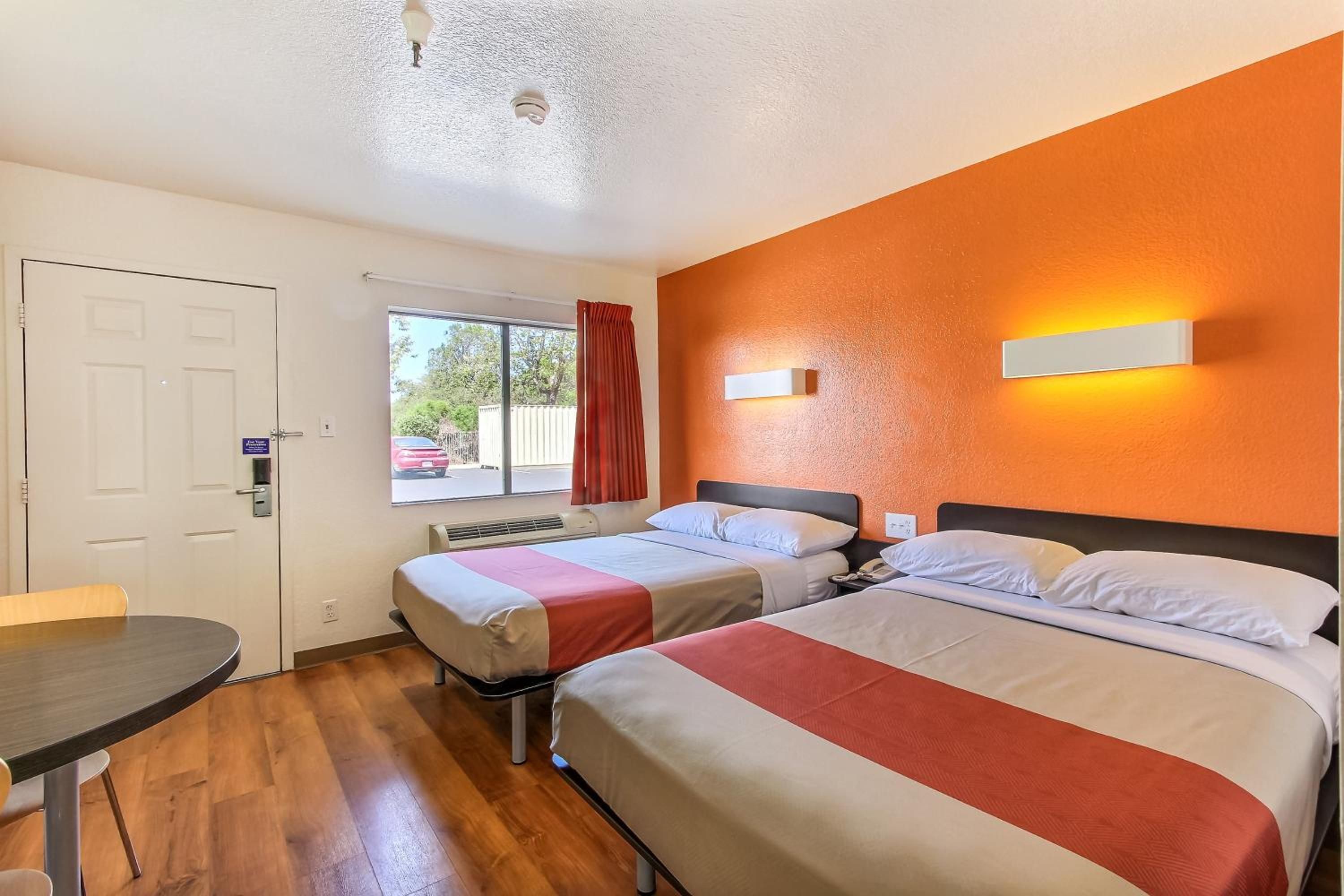 A hotel room with two beds, a desk, and a window with curtains.