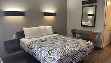 A hotel room with a bed, a small table, and a chair. There are two wall-mounted lights above the bed and a mirror on the wall.