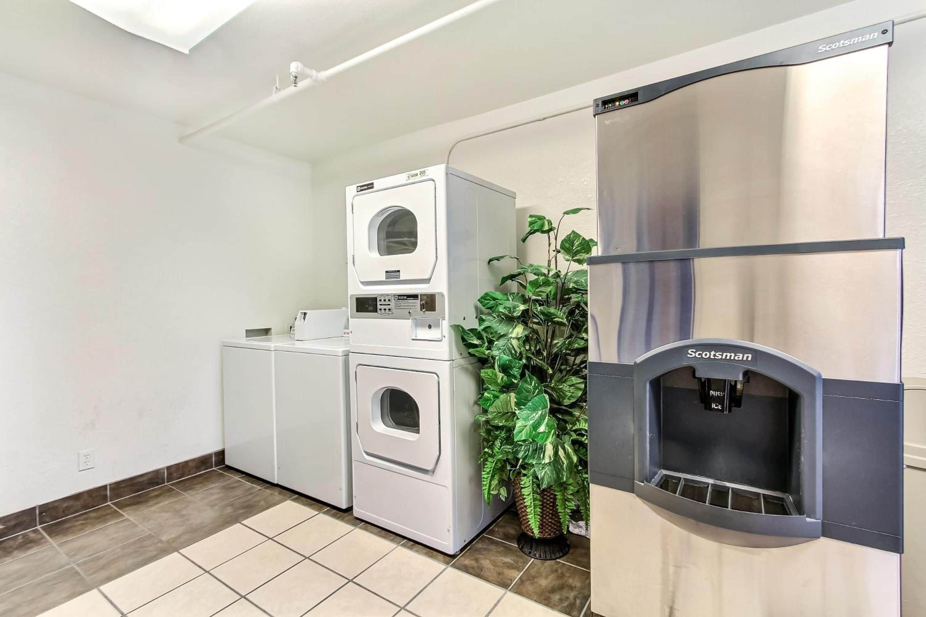A laundry facility with a front-loading washer, a stacked dryer, and a water dispenser.