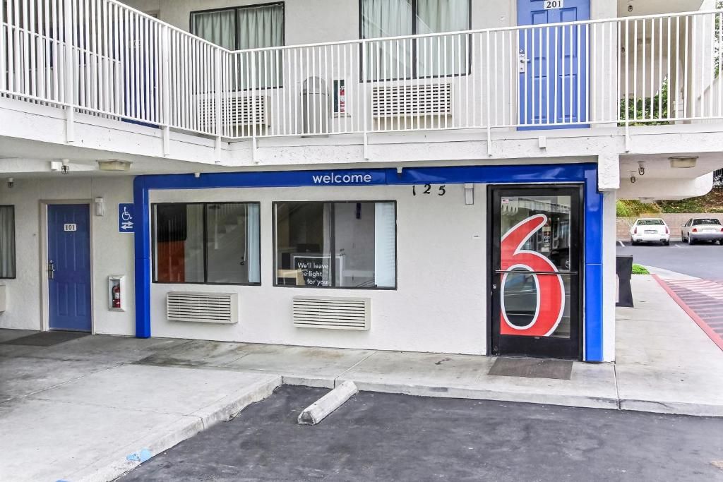L’entrée d’un hôtel, avec une façade bleue et blanche, une pancarte « Bienvenue » et un grand chiffre rouge « 6 » sur la porte.
