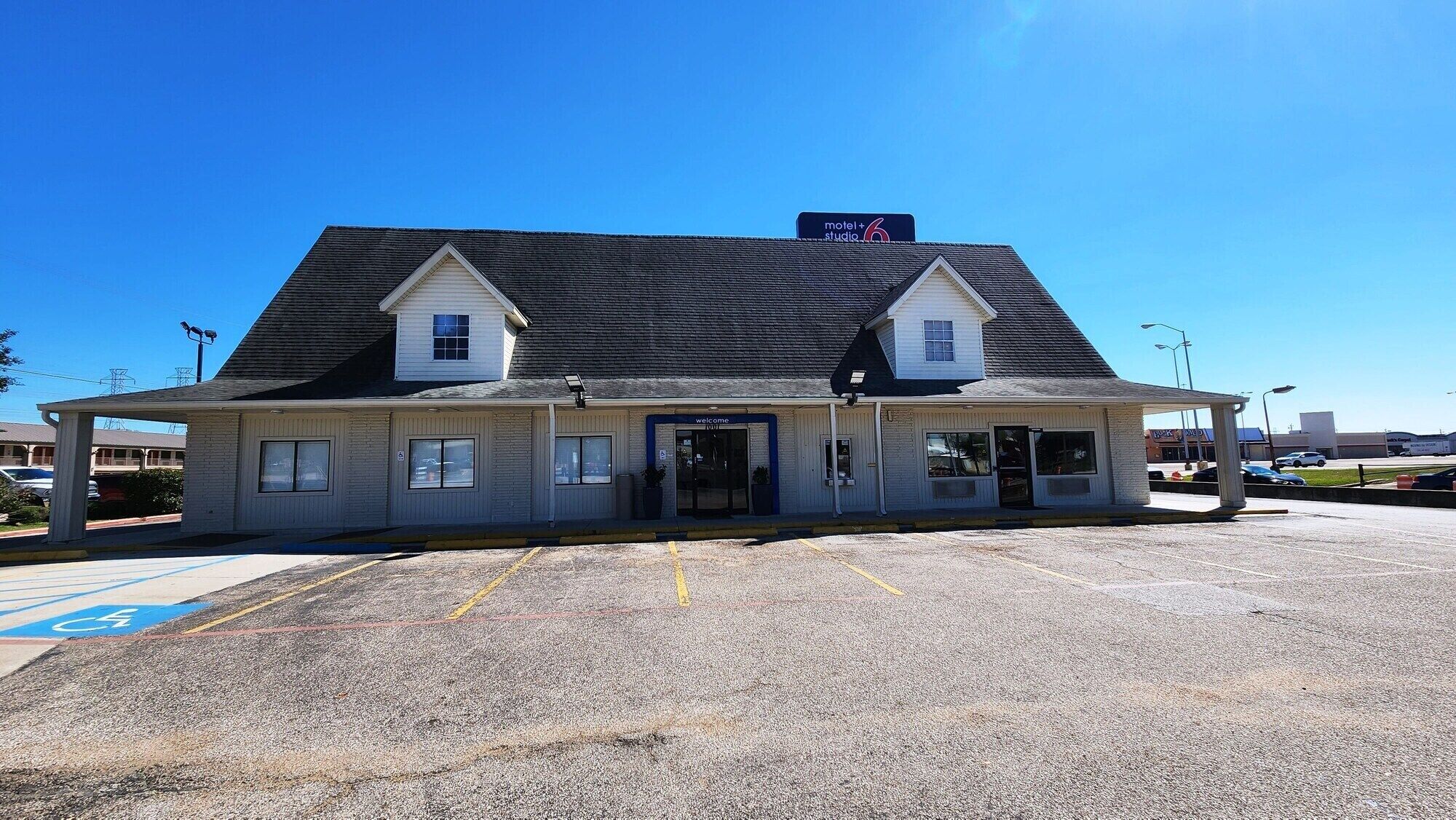 A motel with a simple, single-story structure, a covered parking area, and a clear blue sky.