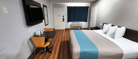 Habitación de hotel con cama, escritorio, silla, televisión y ventana con cortinas.