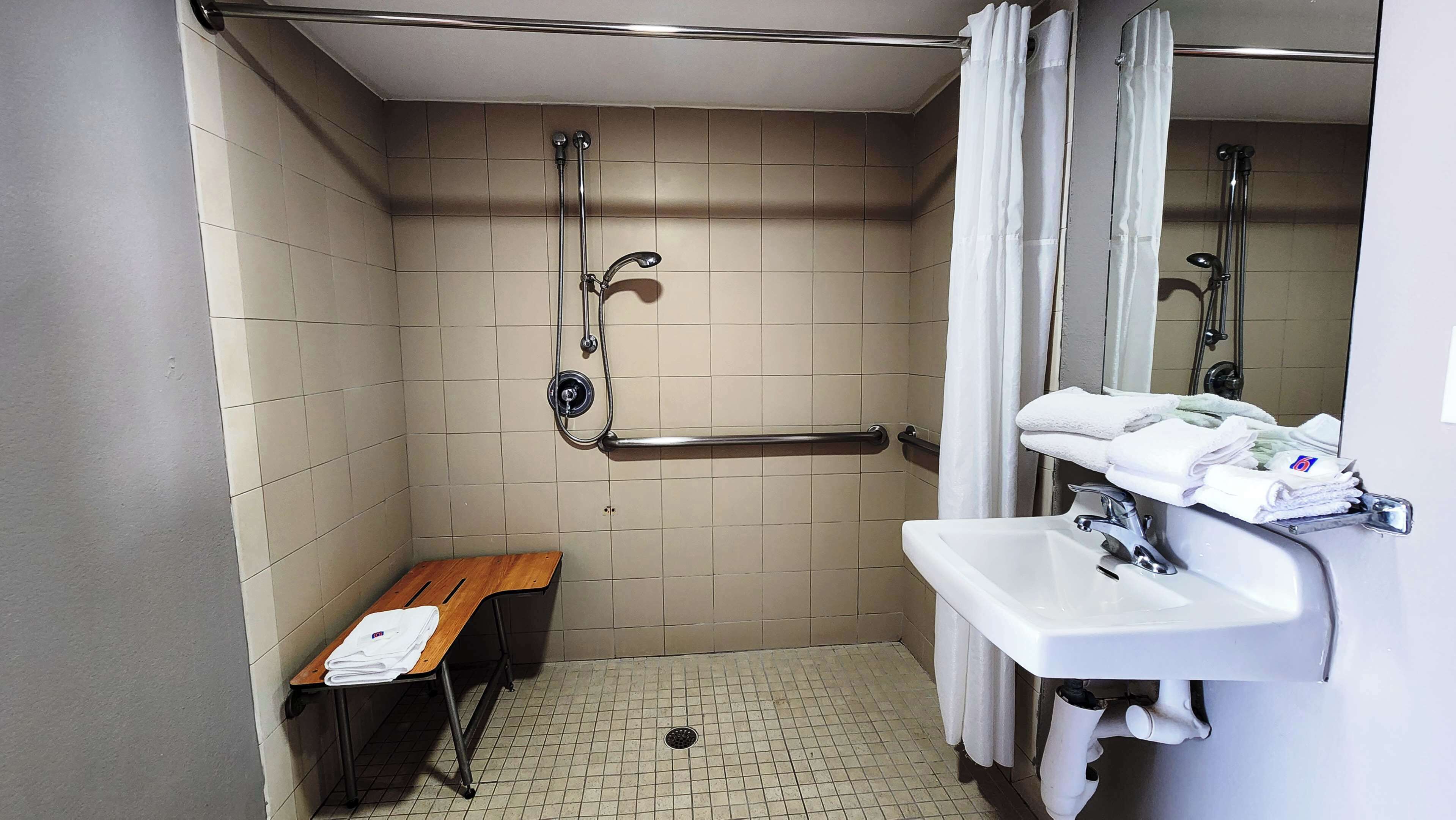 A small, tiled bathroom with a shower, a bench, and a sink with towels.