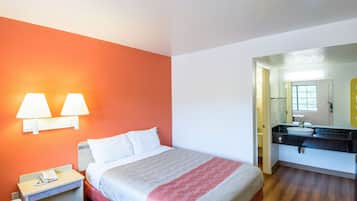 Una habitación de hotel con cama, lámparas de noche, mesita de noche y baño con lavamanos y espejo.