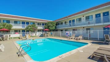 A pool area with lounge chairs and umbrellas, surrounded by a fenced building with multiple balconies.