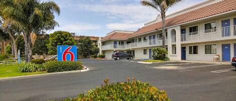 A motel with a central parking area, a sign indicating a nearby location, and a row of rooms with balconies.