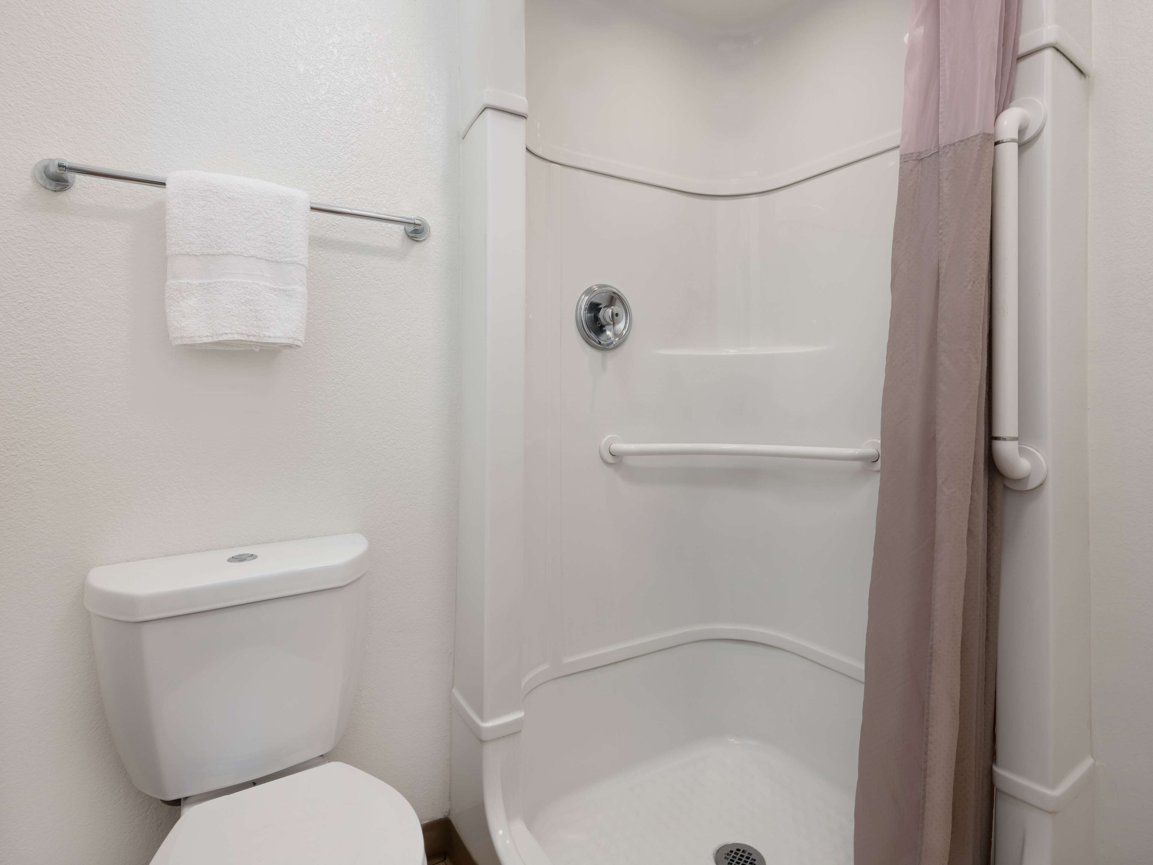 Un baño con inodoro, ducha con barra de apoyo y perchero.