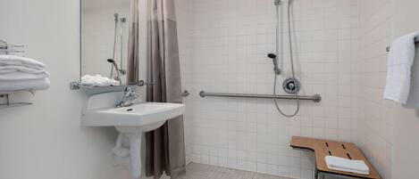 A modern bathroom with a sink, mirror, shower, and grab bar.