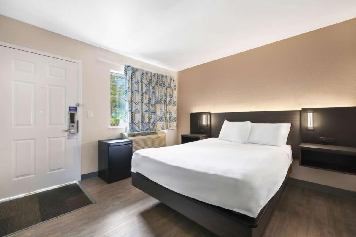 A hotel room with a bed, bedside tables, a door, and a patterned curtain.