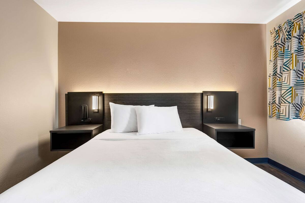 Een hotelkamer met een groot bed, twee nachtkastjes met lampen en een kamer met een patroon op de muur.