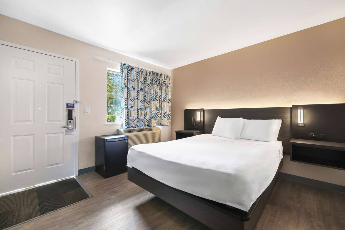 Een moderne hotelkamer met een groot bed, nachtkastjes, een ingebouwde televisie en een kamerbreed gordijn.