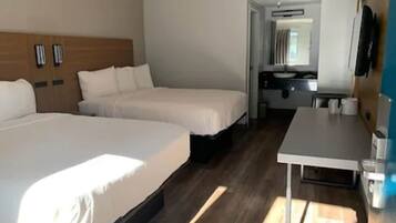 Une chambre d’hôtel avec deux lits, un petit bureau, un miroir et une télévision.