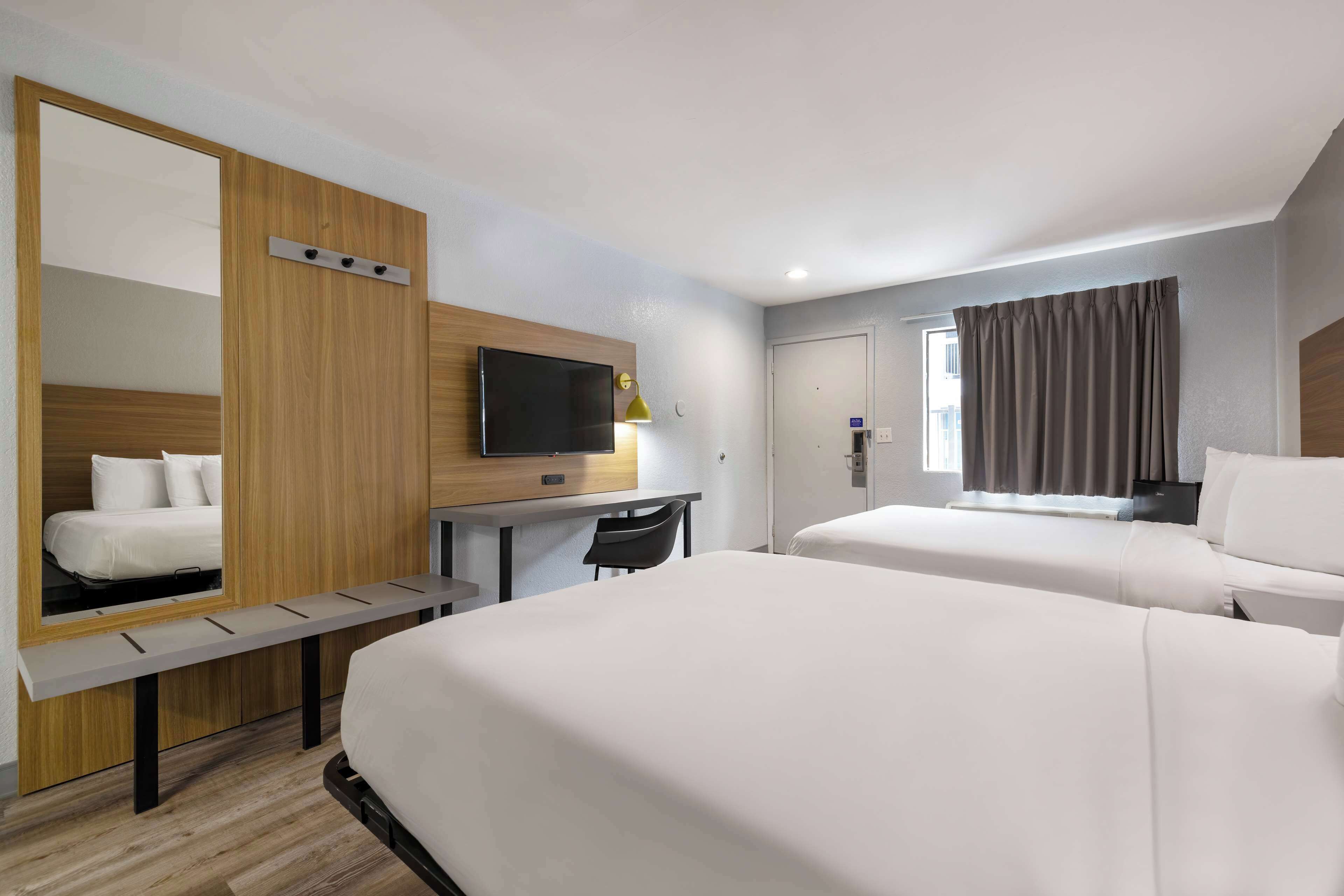 Habitación de hotel con dos camas, un escritorio, una silla, un televisor y un espejo.