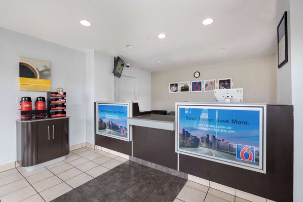 A reception area with a dark wooden desk, a coffee machine, and a clock on the wall. - Motel 6 Santa Ana, CA (Santa Ana)