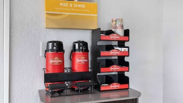 Uma estação de café com duas máquinas de café, uma pilha de xícaras e um letreiro com a inscrição "RISE & SHINE".