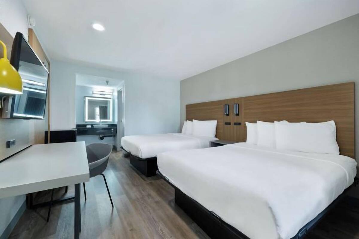 Une chambre d’hôtel avec deux lits, un bureau, une chaise et une télévision.