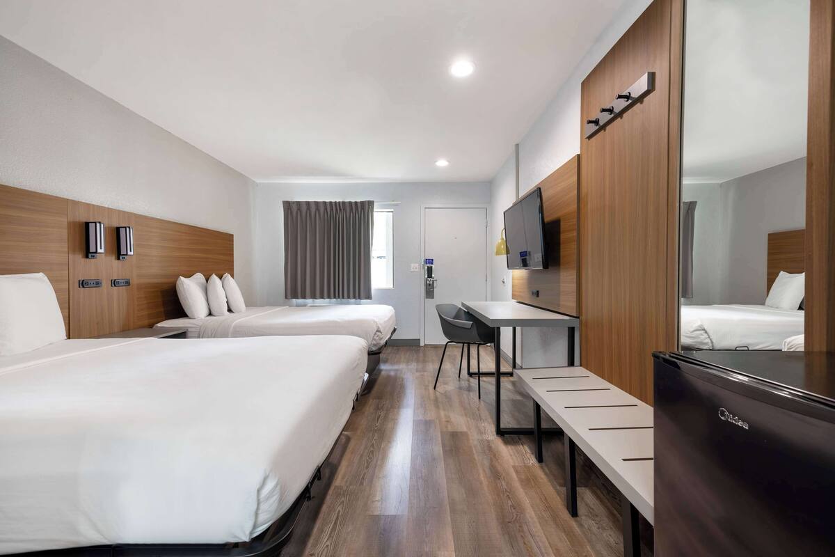 Une chambre d’hôtel avec deux lits, un bureau, un miroir, une télévision et un réfrigérateur.