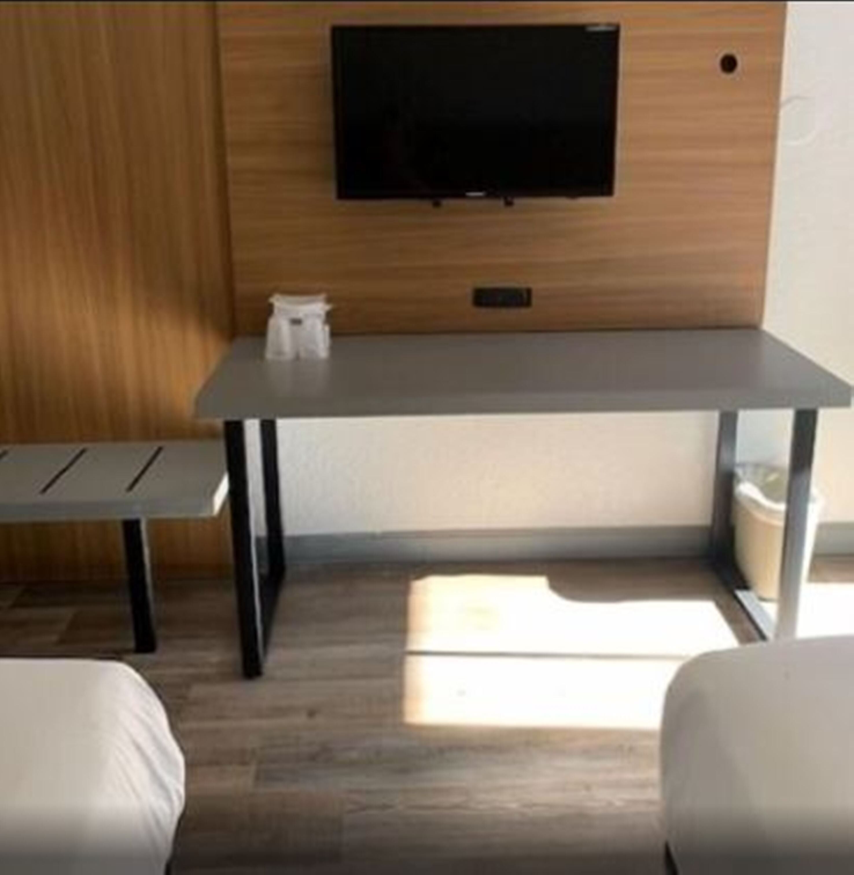 A modern room with a wooden wall, a flat-screen TV mounted above a gray table, and two white beds.