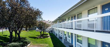 A multi-story motel with a central courtyard, featuring a well-maintained lawn and trees.