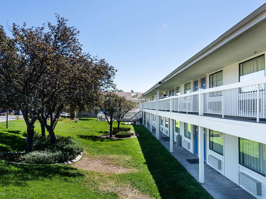Um motel com vários andares e um pátio central, com um gramado bem cuidado e árvores.