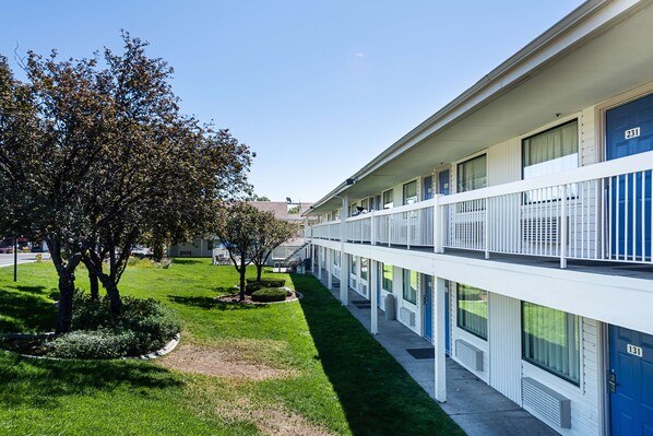 A multi-story motel with a central courtyard, featuring a well-maintained lawn and trees. - Motel 6 Sparks, NV - Airport - Sparks (Sparks)
