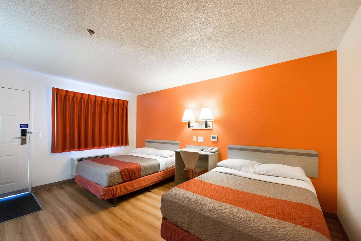 A hotel room with two beds, orange walls, a window with orange curtains, and a door with a sign.
