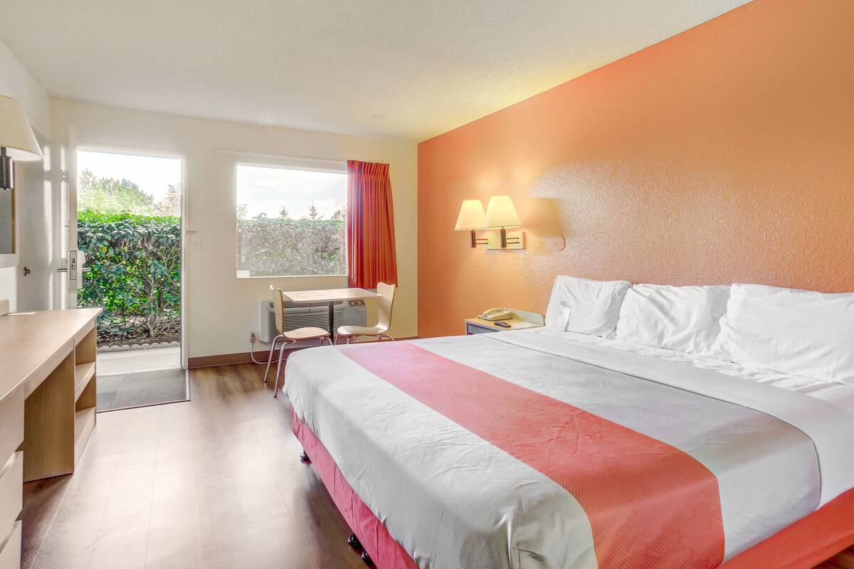 A hotel room with a bed, desk, chair, and a window with a view of greenery.