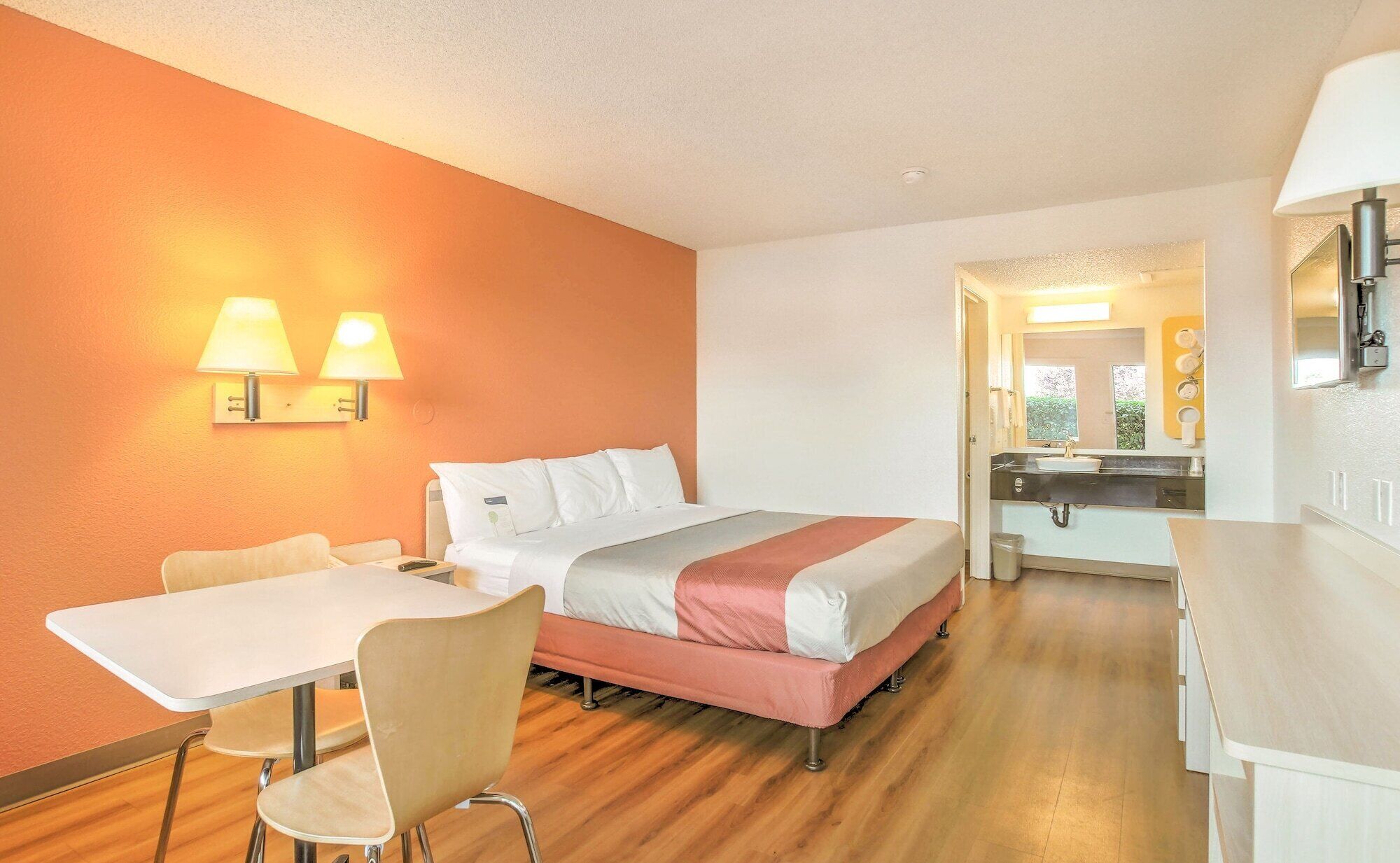 A hotel room with a bed, a desk, a chair, and a bathroom visible through an open door.