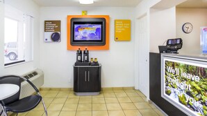 A reception area with a digital screen displaying weather information, a clock, and a sign promoting travel savings. - Motel 6 Medford, OR - North (Medford)