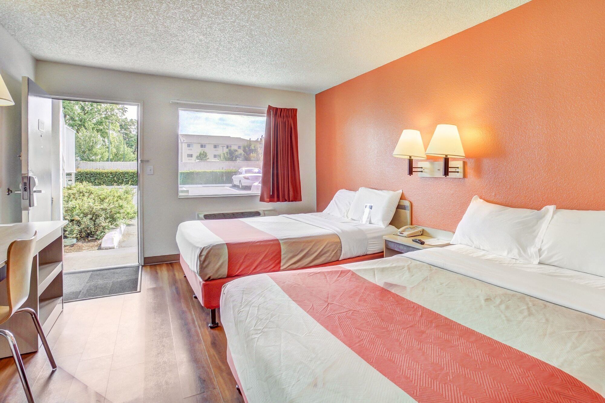 A hotel room with two beds, a desk, and a window with a view of the outside.