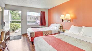 A hotel room with two beds, a desk, and a window with a view of the outside.
