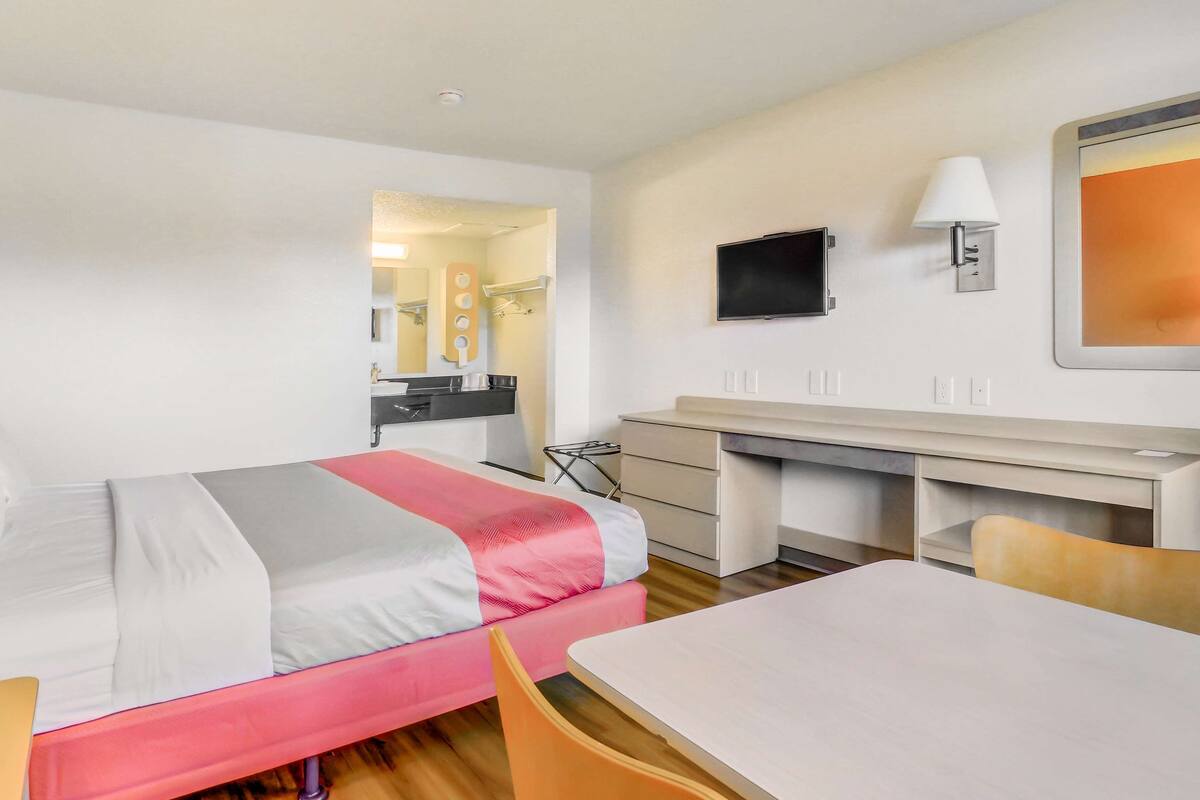 A hotel room with a bed, a desk, a chair, a TV, and a mirror.