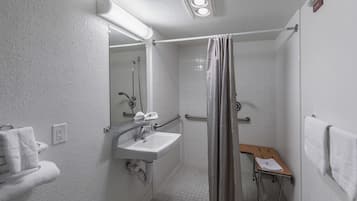 A small, white bathroom with a sink, mirror, and shower.