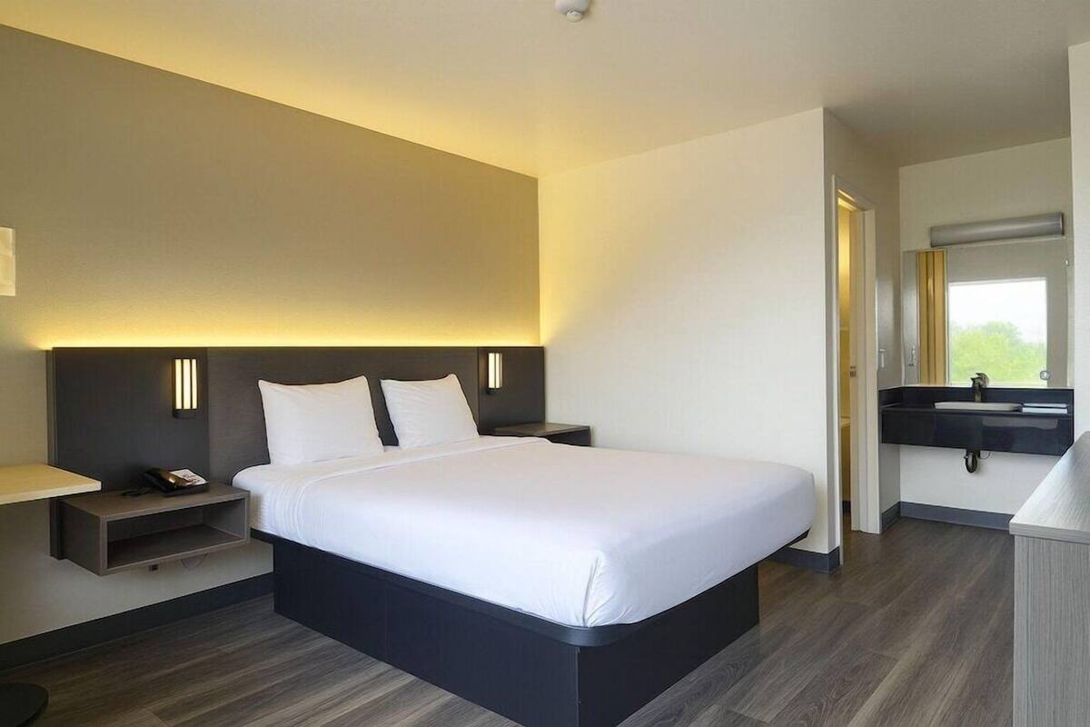 Een moderne hotelkamer met een groot bed, nachtkastjes, een inbouw bureau en een badkamer met een wastafel en spiegel.