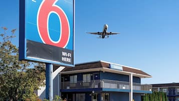 A motel sign with a large '6' and 'Wi-Fi here' text, a building with a 'Welcome' sign, and a plane flying in the background.