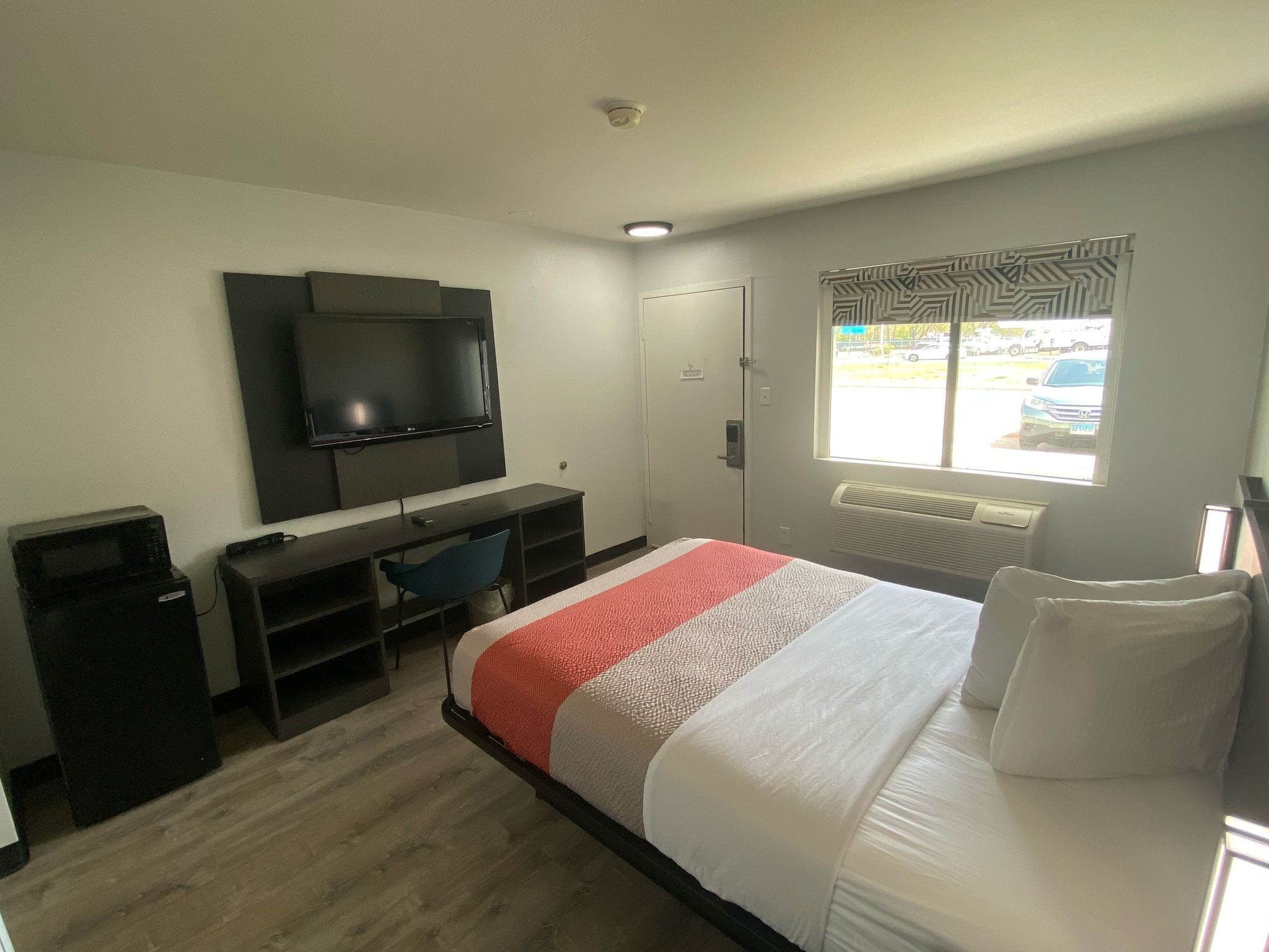 A hotel room with a bed, a desk, a chair, a television, and a window with a view of the outside.