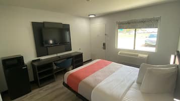 A hotel room with a bed, a desk, a chair, a television, and a window with a view of the outside.
