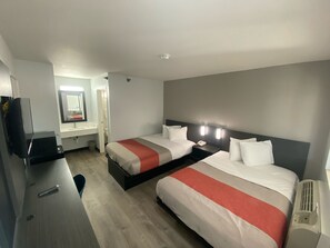 Une chambre d’hôtel avec deux lits, un bureau, un miroir et une télévision.