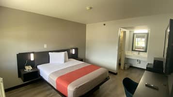 A hotel room with a bed, bedside tables, a desk, a chair, and a bathroom visible through an open door.