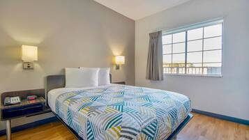 Una habitación de hotel con cama, mesita de noche, lámpara y ventana con cortinas.