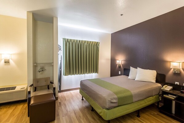A hotel room with a bed, bedside lamps, a heater, a chair, and a window with curtains. - Studio 6 Mcallen, TX (McAllen)