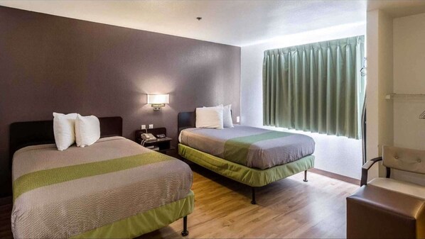 Habitación de hotel con dos camas, una mesita de noche, un escritorio, una silla y una ventana con cortinas.