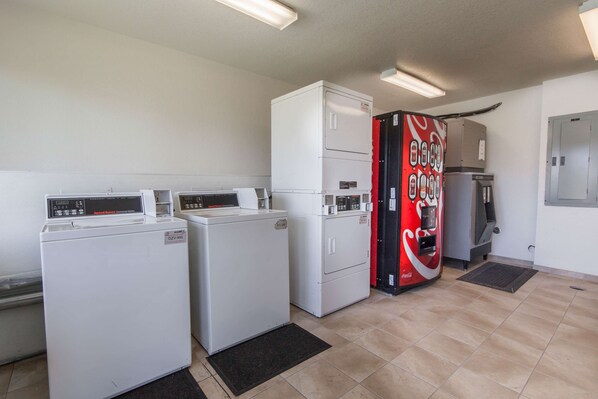 A laundry room with two dryers, a washing machine, and a Coca-Cola vending machine. - Studio 6 El Paso, TX - East (El Paso)