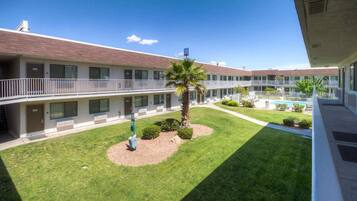 A multi-story motel with a central courtyard featuring a palm tree, a swimming pool, and well-maintained lawns.