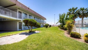 A hotel with a well-maintained lawn, neatly trimmed bushes, and a swimming pool area. - Studio 6 El Paso, TX - East (El Paso)