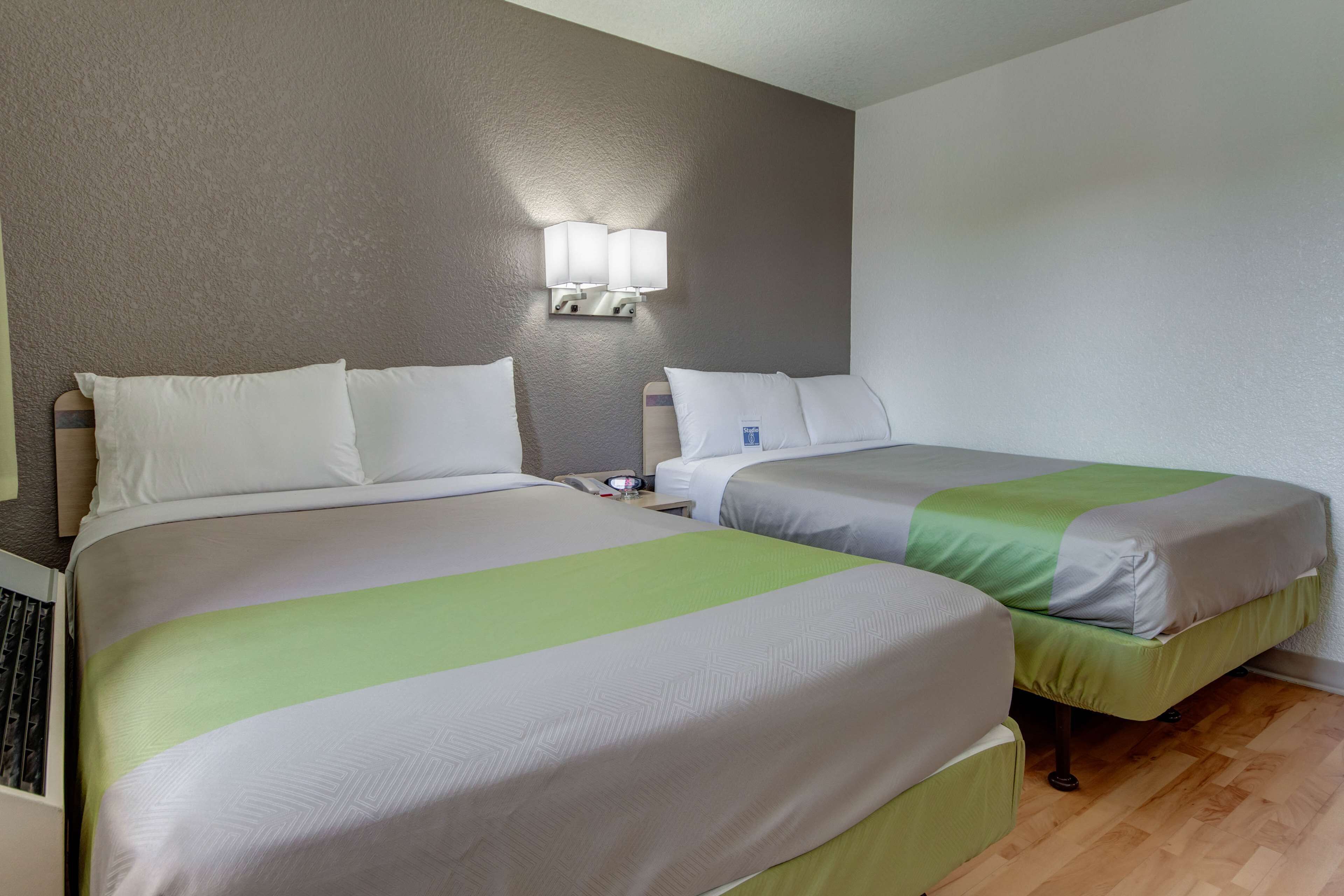 A hotel room with two beds, a nightstand with a lamp, and a wooden floor.